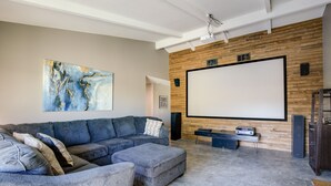 A modern living room with a sectional sofa, ottoman, and a large flat-screen TV mounted on a wooden wall. - Theater Room & Pool Deck: Retreat in Palm Desert! (Palm Desert)