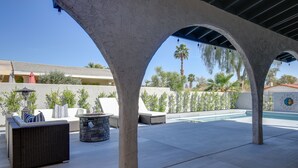 An outdoor patio with a pool, covered seating area, and a stone fire pit. - Theater Room & Pool Deck: Retreat in Palm Desert! (Palm Desert)