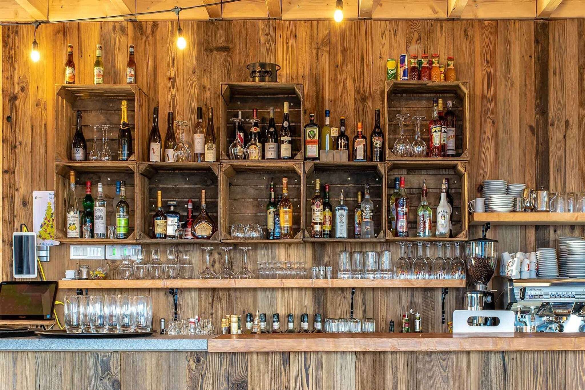 A bar area with wooden shelves stocked with various bottles and glasses.
