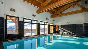 A swimming pool with large windows offering mountain views, wooden beams on the ceiling, and a small staircase leading to an upper level. - Cozy Mountain Stay w/ Balcony (Arâches-La-Frasse)