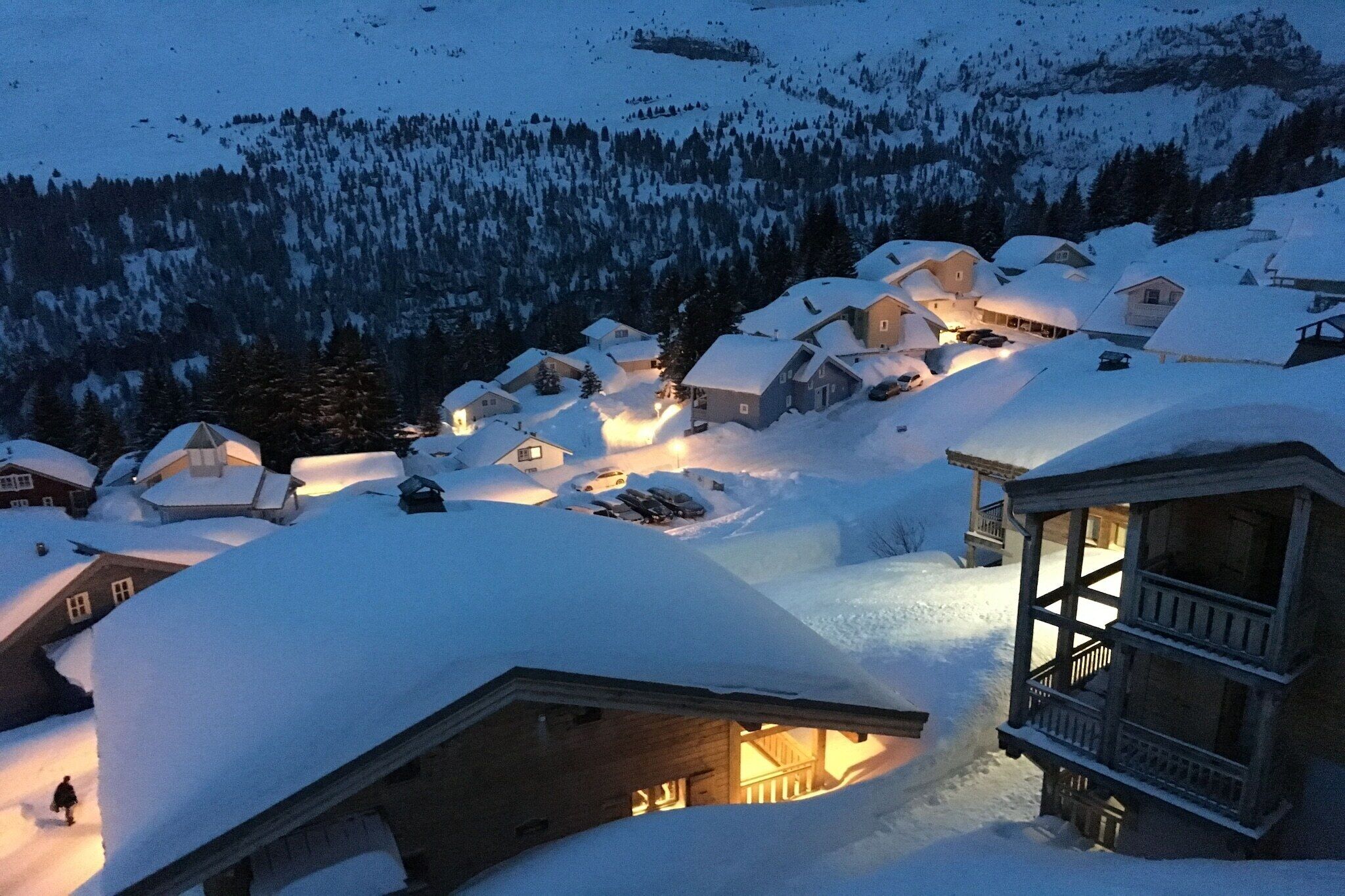 A snow-covered village with wooden houses, a wooden structure with a balcony, and a lit interior.