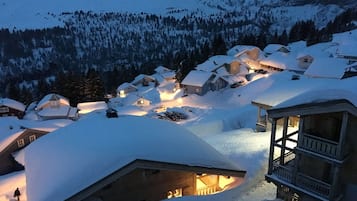 A snow-covered village with wooden houses, a wooden structure with a balcony, and a lit interior.
