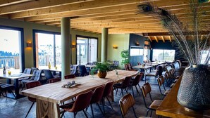 A spacious indoor dining area with wooden tables and chairs, large windows, and a decorative plant centerpiece. - Cozy Mountain Stay w/ Balcony (Arâches-La-Frasse)