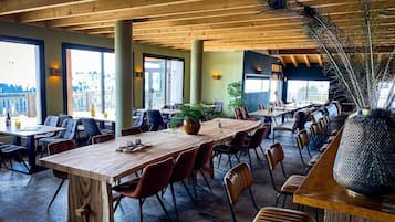 Un'ampia sala da pranzo interna con tavoli e sedie in legno, grandi finestre e un'elegante composizione floreale al centro.