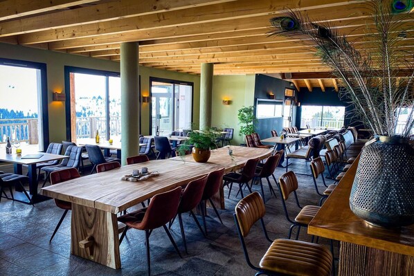 A spacious indoor dining area with wooden tables and chairs, large windows, and a decorative plant centerpiece. - Cozy Mountain Stay w/ Balcony (Arâches-La-Frasse)