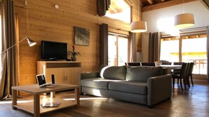 Een gezellige woonkamer met een bank, salontafel, televisie en een eethoek met tafel en stoelen.