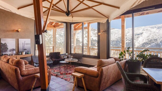 Een gezellige kamer met een bank, stoelen, een tafel en uitzicht op besneeuwde bergen.