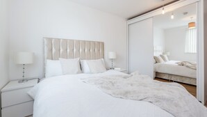 Un dormitorio moderno con una cama grande, una mesita de noche con lámpara y un espejo en la pared.
