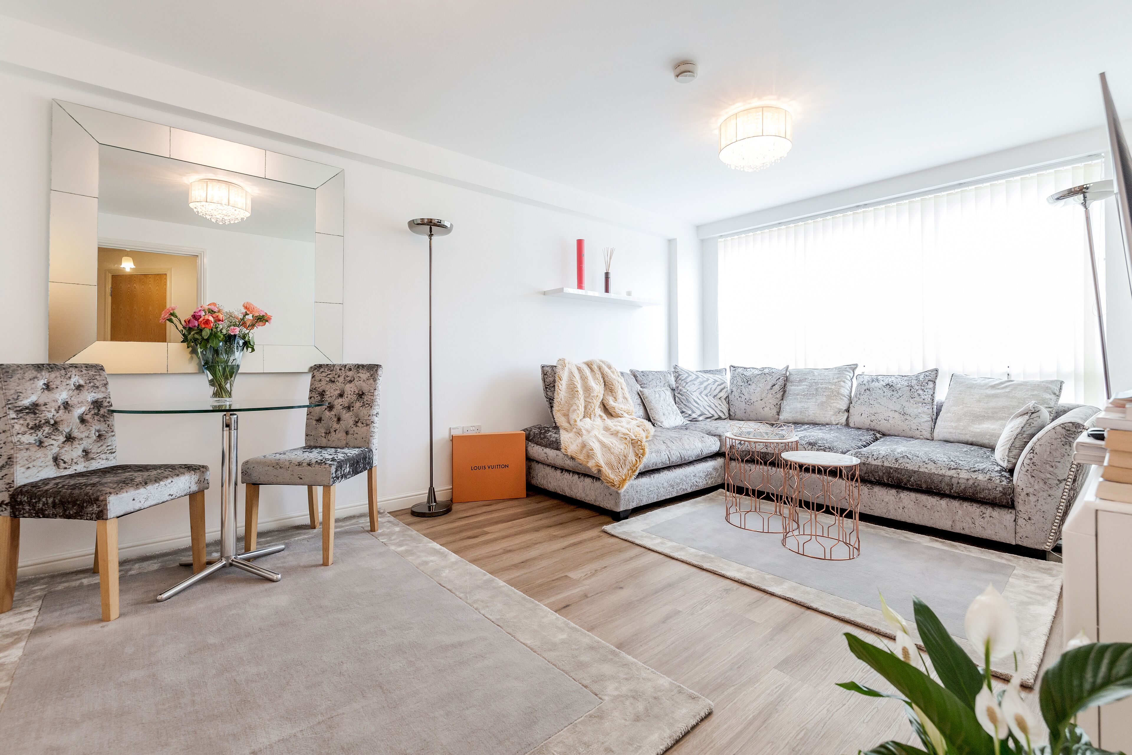 A modern living room with a glass dining table, two chairs, a sofa, and a floor lamp.