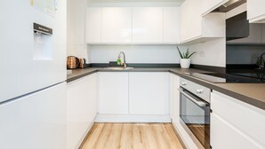 Una cocina moderna con armarios blancos, un lavamanos de acero inoxidable, horno empotrado y suelo de madera.