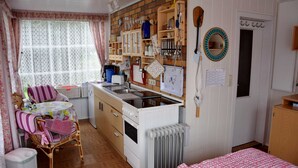 A cozy kitchen with wooden cabinets, a stove, and a dining area with wicker chairs and a table. - Ferienhaus Schmidt, Erika - Ferienhaus 7 (Mönkebude)