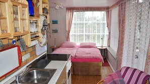 A compact bedroom with a bed, a small bedside table, a chair, and a kitchenette area with a sink and cabinets. - Ferienhaus Schmidt, Erika - Ferienhaus 7 (Mönkebude)