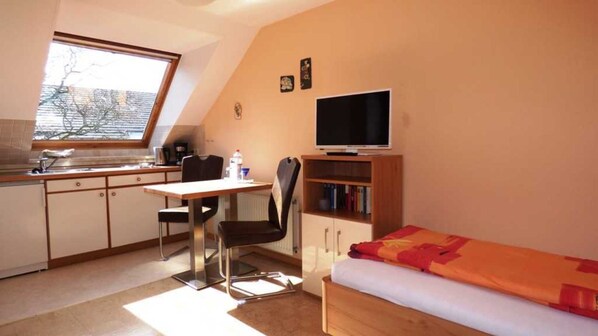 A compact room with a kitchenette, a dining area, a bed, and a television.