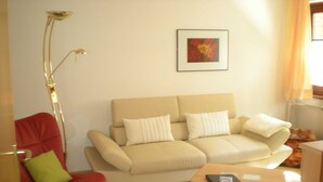 Un salon moderne avec un canapé beige, un fauteuil rouge, une petite table en bois et un lampadaire.