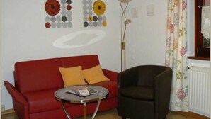 Une pièce avec un canapé rouge, un fauteuil noir, une petite table ronde et un lampadaire.