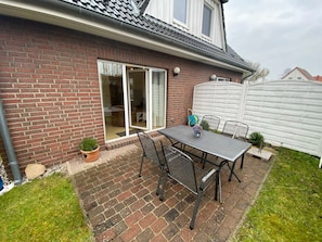 A patio with a table and chairs, a sliding glass door, and a brick wall.