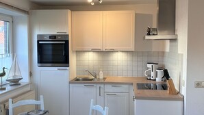 A compact kitchen with white cabinets, a built-in oven, a coffee maker, and a knife block on the countertop.