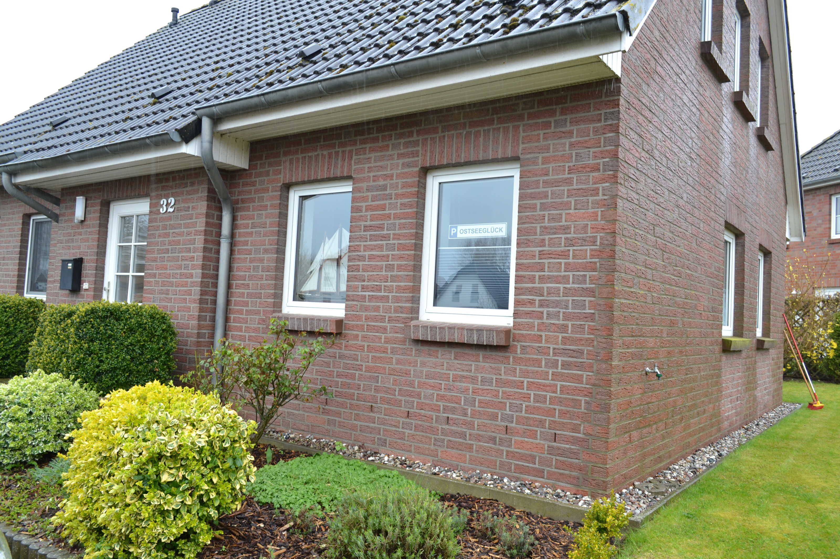 A brick house with three windows, a mailbox, and a small garden with various plants.