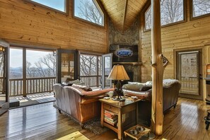 A wooden cabin interior with a fireplace, leather sofas, a coffee table, and a bookshelf. - A Golden Retreat | Morganton, GA (Morganton)