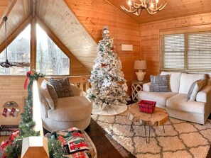 A cozy log cabin interior with a Christmas tree, a sofa, a chair, and a small table. - A Golden Retreat | Morganton, GA (Morganton)