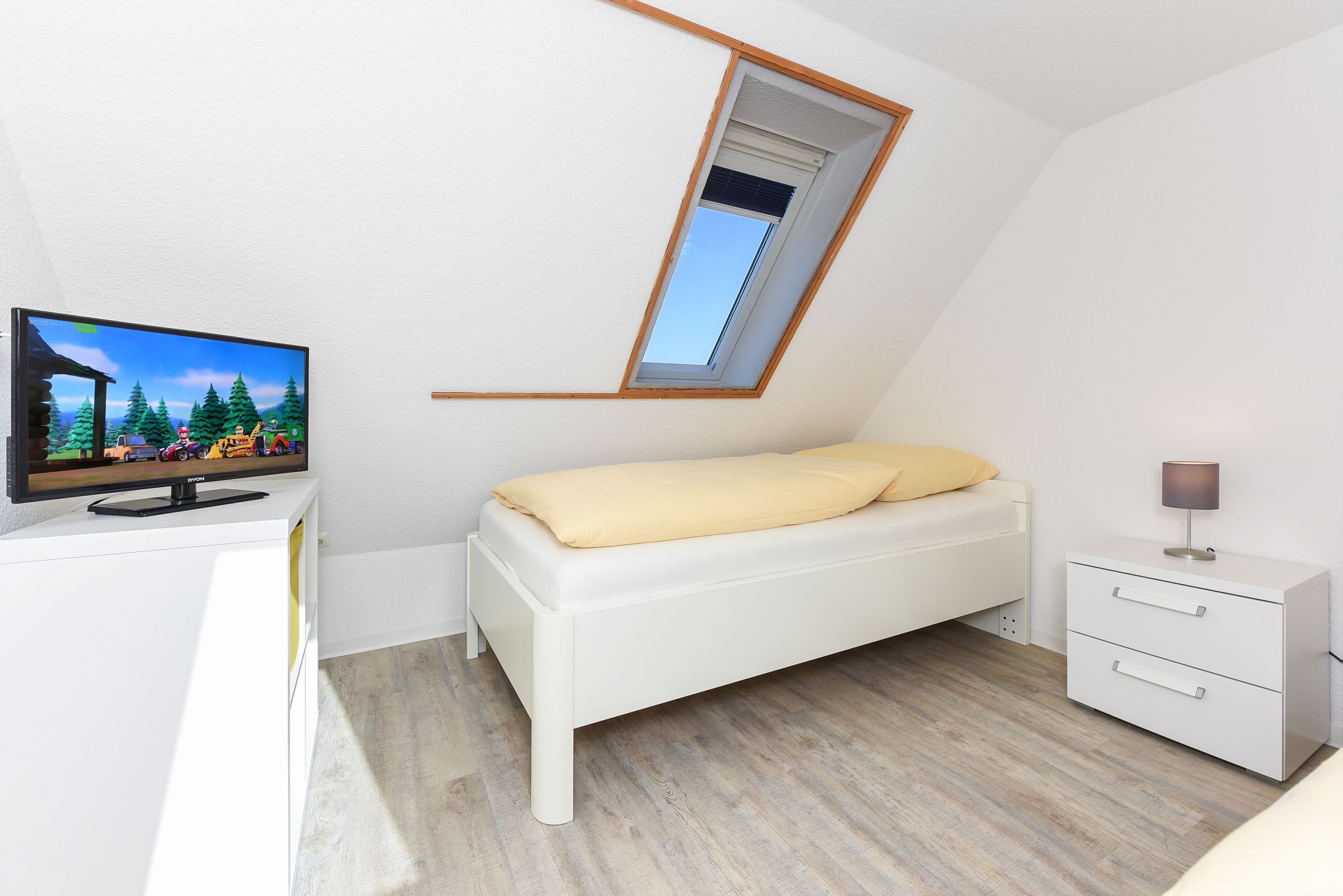 Une chambre avec un plafond en pente, un lit, une télévision et une petite table de chevet.