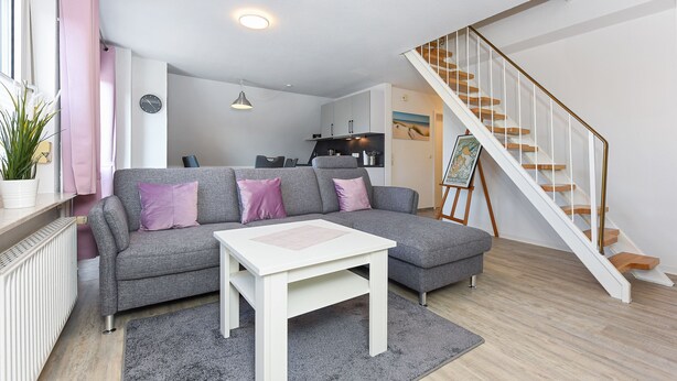 A modern living room with a grey sofa, white coffee table, and a staircase leading to a loft area. - Ferienwohnung Brise - Mein Urlaubshaus (Esens)