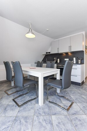 A modern kitchen with white cabinets, a white countertop, and a dining area with a white table and grey chairs.