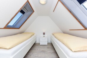 A small, triangular room with two beds, a nightstand, and a skylight.