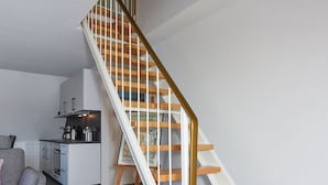 A modern interior with a wooden staircase, a kitchen area, and a grey sofa. - Ferienwohnung Brise - Mein Urlaubshaus (Esens)