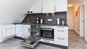 A modern kitchen with white cabinets, a built-in dishwasher, and an oven. - Ferienwohnung Brise - Mein Urlaubshaus (Esens)
