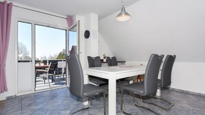 A dining area with a white table and four grey chairs, a ceiling light, and a view through a glass door. - Ferienwohnung Brise - Mein Urlaubshaus (Esens)