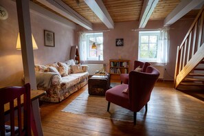 A cozy living room with a floral sofa, a red armchair, a wooden floor, and a bookshelf.