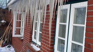 Ein Backsteinhaus mit von der Dacheindeckung hängenden Eisblumen, Schnee auf dem Boden und einem Fenster mit weißem Rahmen.