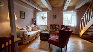 Ein gemütliches Wohnzimmer mit einem blumigen Sofa, einem roten Sessel, Holzboden und einem Bücherregal.