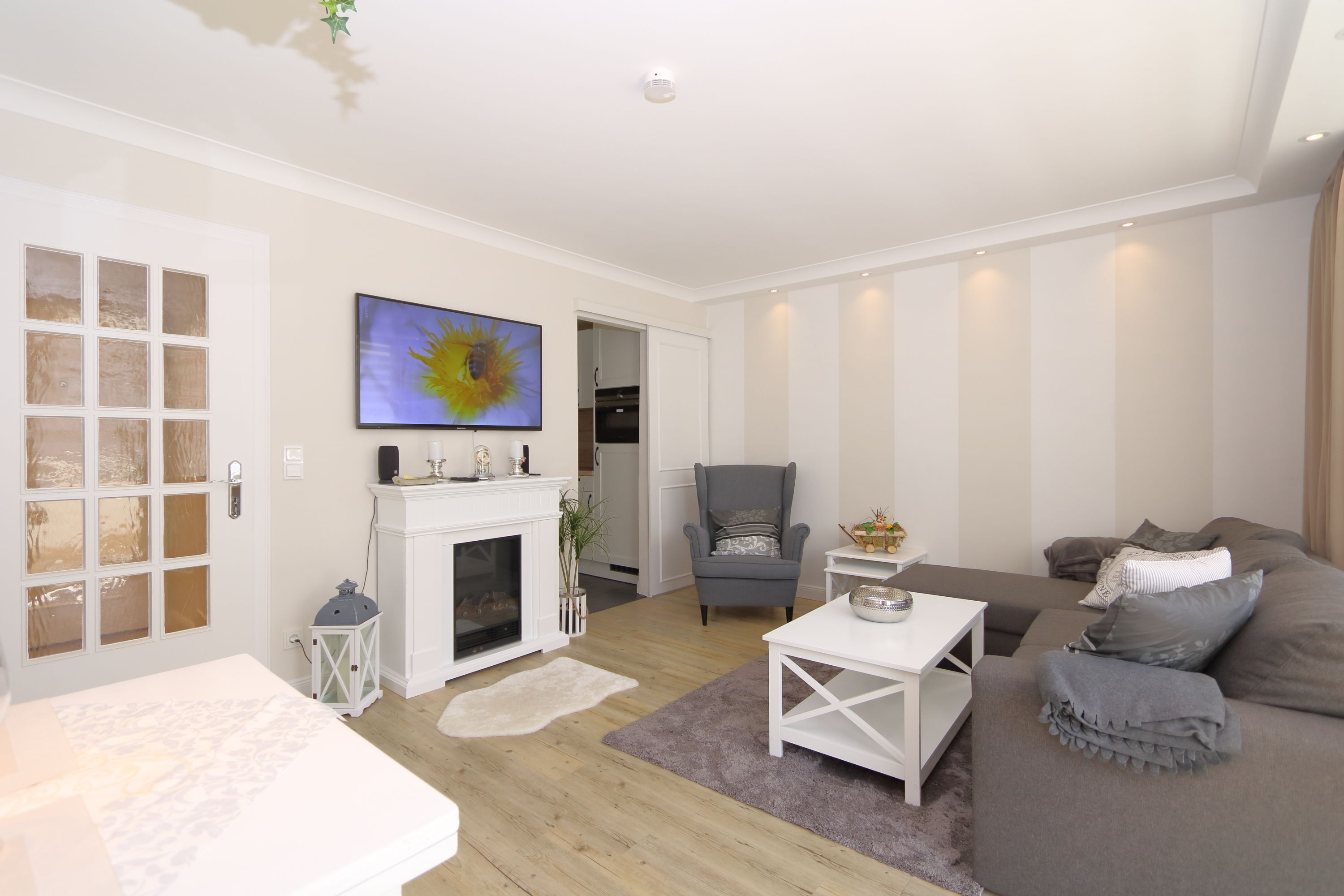 A modern living room with a fireplace, a flat-screen TV, a grey armchair, and a grey sofa.