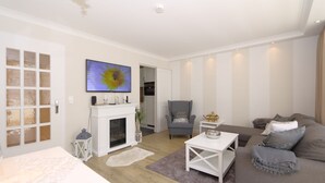 Een moderne woonkamer met een open haard, een flatscreen televisie, een grijze fauteuil en een grijze bank.