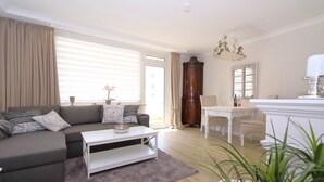 Een moderne woonkamer met een grijze bank, een witte salontafel, en een eethoek met een witte tafel en stoelen.