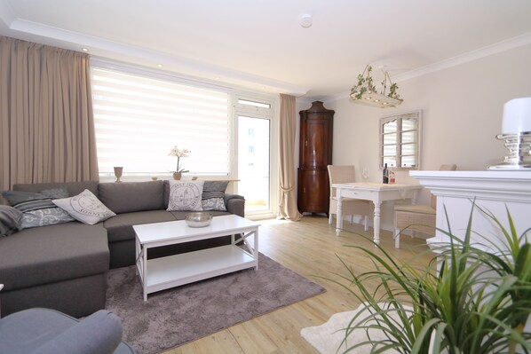 A modern living room with a grey sofa, white coffee table, and a dining area with a white table and chairs.