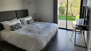 Ein modernes Schlafzimmer mit einem großen Bett, einem Schreibtisch und Blick auf einen Garten.
