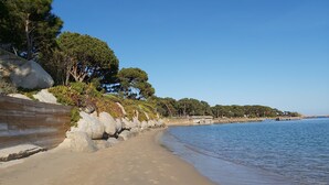 Ein Strand mit einem Holzsteg, großen Felsen und Bäumen.