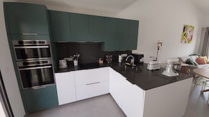 Una cocina moderna con armarios azul verdoso, encimera negra y electrodomésticos de acero inoxidable.