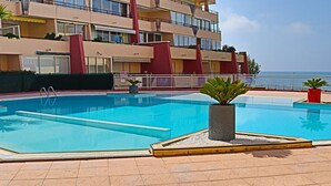 A swimming pool with a tiled deck, surrounded by a building with balconies and a view of the sea. - Top floor apartment in Sète for 6 people (Sète)