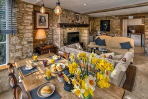 A cozy room with stone walls, a fireplace, a sofa, and a dining table set for breakfast. - The Little Window, Classic Cotswolds Cottage (Gloucestershire)