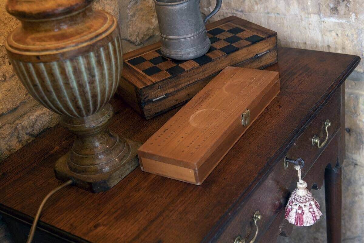 A wooden chest of drawers with a metal lamp and a chessboard on top.
