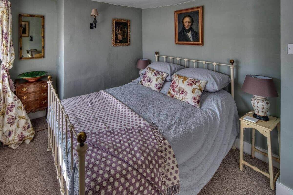 A bedroom with a bed, a dresser, a mirror, a lamp, and a painting on the wall.