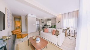 Een moderne woonkamer met een bank, salontafel en stoelen. Een keuken met een eettafel en stoelen is ook aanwezig.