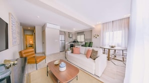 A modern living room with a sofa, coffee table, and chairs. There is a kitchen area with a dining table and chairs.