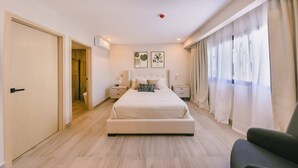 A bedroom with a large bed, bedside tables, a chair, and a door leading to another room.