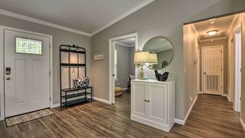 Un couloir avec un plancher en bois, une porte blanche, un banc en métal noir, une armoire blanche et un miroir au mur.