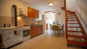 Una cocina con estufa, horno y armarios de madera. Hay una mesa de comedor con sillas y una escalera de madera.